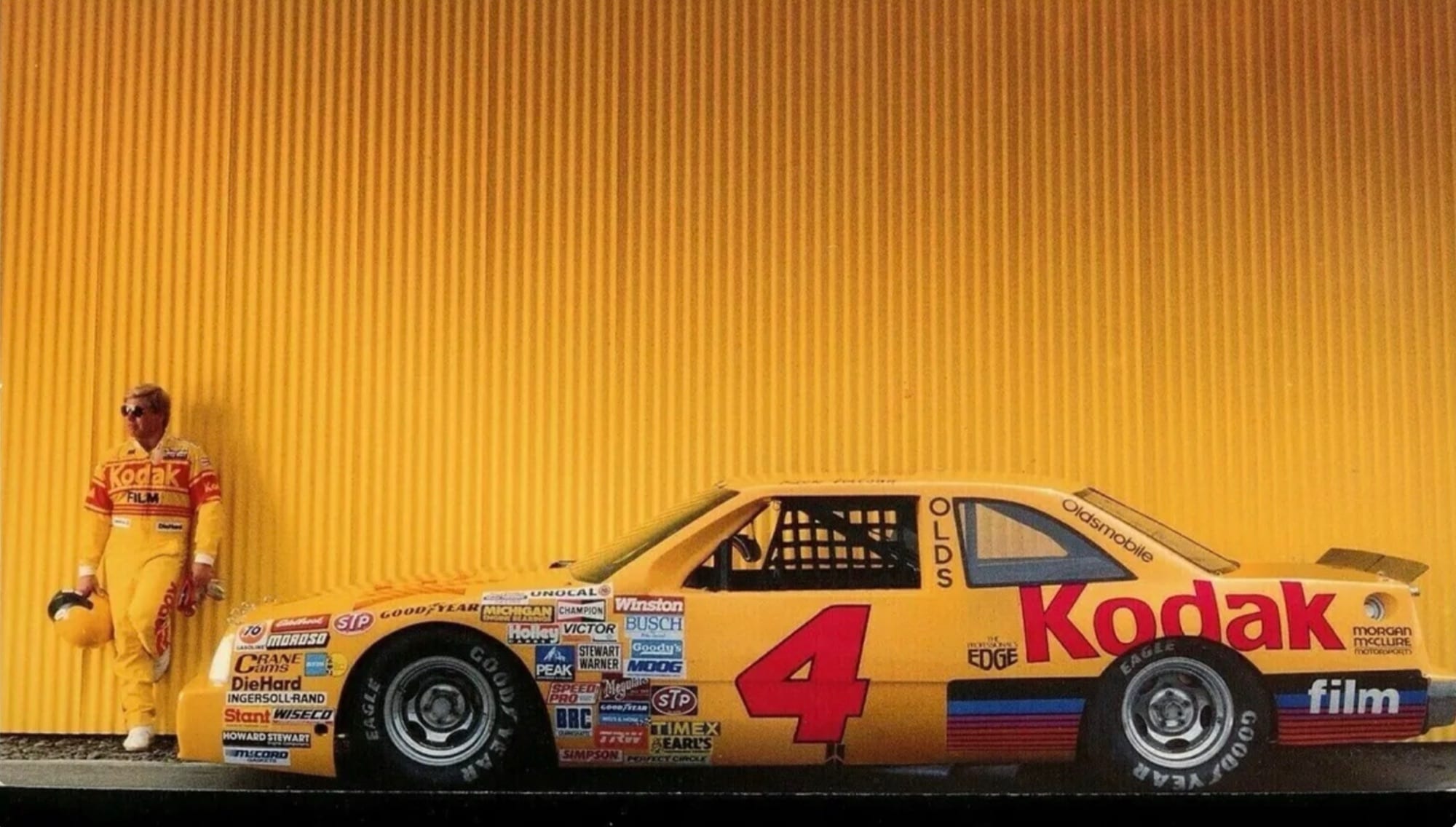 Rick Wilson in his driving suit beside his No. 4 NASCAR Cup Series car